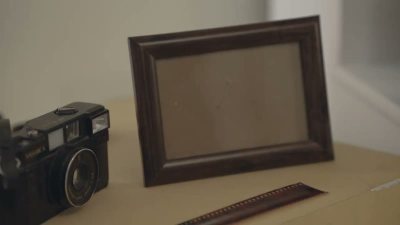 An empty wooden picture frame beside an old camera on a desk.