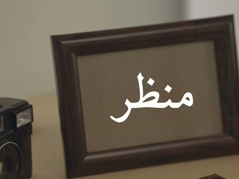 A camera and a picture frame on a desk, the Urdu word Manzar over them.